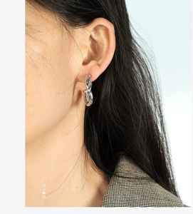 Close-up of twisted rope texture on silver C-shaped hoop earrings worn by a model