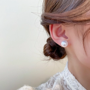 Close-up of a model wearing a large round white pearl stud earring with a glossy finish
