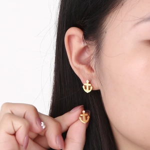 Detail of gold anchor earrings with white rhinestone worn by model on white background