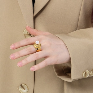 Dettaglio di un elegante anello d'oro con perla bianca su un blazer kaki