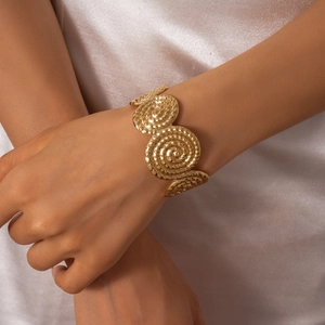 Détail de trois disques spirales dorés sur un large bracelet manchette texturé