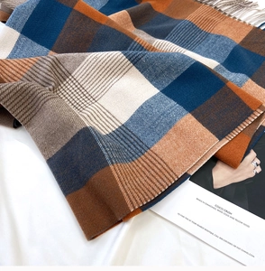 Detailed view of British style navy and orange plaid knit scarf with soft tassel edges