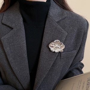 Detail of silver orchid brooch pinned on a grey blazer showcasing metallic texture