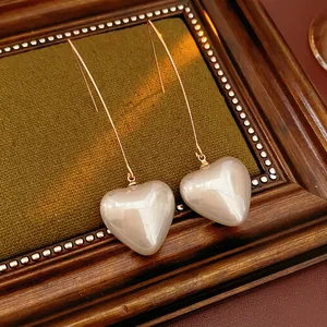 Vintage heart pearl drop earrings with long gold hooks on a luxury green background
