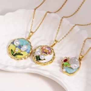 Elegant floral enamel and freshwater pearl pendants on golden necklaces in a shell tray