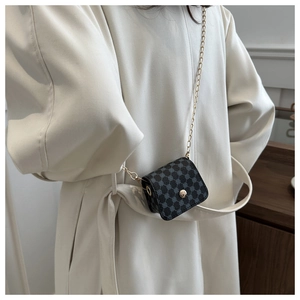 Close-up of a small black crossbody bag with geometric texture and golden chain strap
