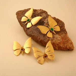 Golden dragonfly jewelry with natural green and brown stones on a rustic stone background