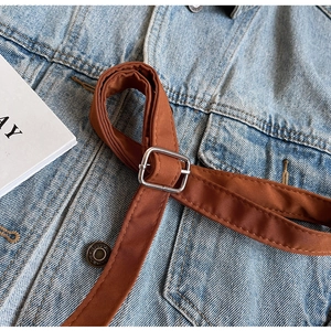 Detail of blue denim fabric featuring a brown woven belt and silver square buckle