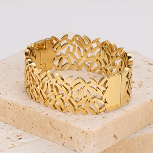 Detailed close-up of a gold hollow leaf pattern bracelet on a beige stone base