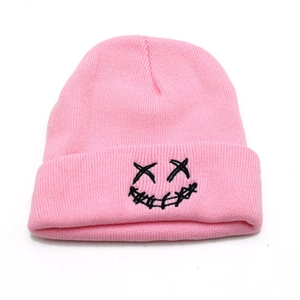 Close-up of pink knitted beanie featuring detailed black embroidered smiley face design