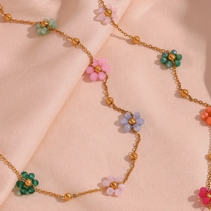 Close-up of golden link necklace with colorful hand-woven beaded flowers on pink silk