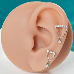 Détail de boucles d'oreilles papillon avec chaînette et clous cœur sur modèle en silicone