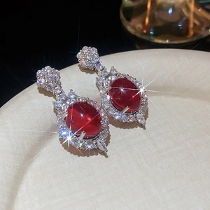 Close-up of red oval flower stud earrings with shimmering crystals on a white tray