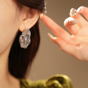 Close-up of model wearing silver twisted hollow geometric hoop earring with retro patterns