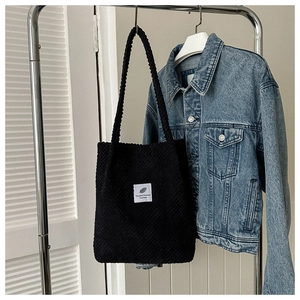 Detail of black waffle pattern tote bag featuring a white logo patch on a denim background
