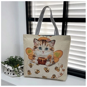 Detail of cute cat and bee embroidery on cream canvas tote bag with striped handles