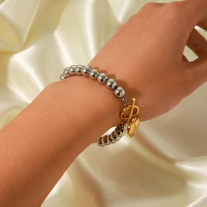 Close-up of silver beaded bracelet with golden heart pendant on model's wrist