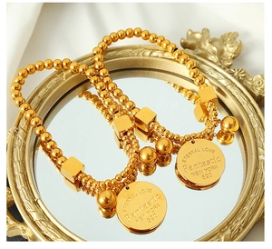Detail view of gold beaded bracelets with engraved charms on a mirror surface