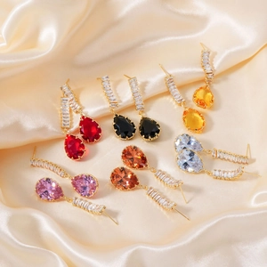 Macro shot of colorful pear-cut zircon earrings on champagne silk fabric background