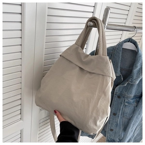 Detail of a beige lightweight nylon handbag with wide handles paired with a denim jacket