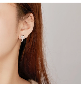 Macro side view of silver cobra snake hoop earrings worn on ear showing sleek metal details