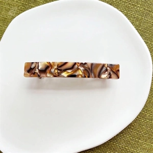 Close-up of a tortoiseshell acetate hair clip on a white ceramic tray with a green background