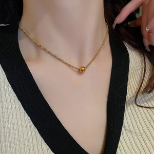 Detail shot of a polished gold bead pendant necklace on a delicate link chain for women