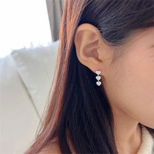 Close-up of triple heart dangle earrings in silver finish worn by a model
