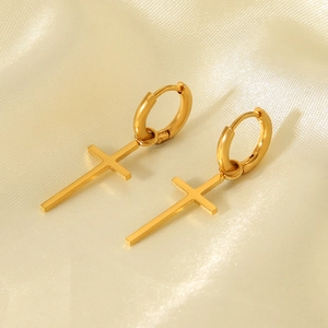 Close-up of golden stainless steel cross earrings on elegant beige silk fabric