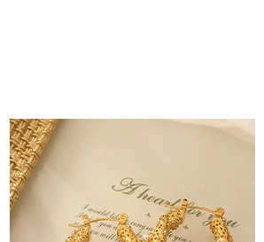 Détail d'une boucle d'oreille créole dorée texturée sur une carte avec texte manuscrit