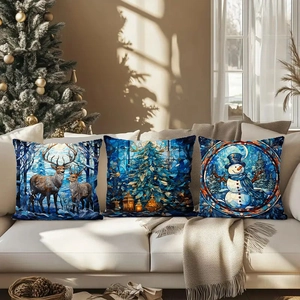 Three square Christmas pillowcases with blue stained glass deer and snowman prints on sofa