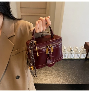 Detail of burgundy leather box bag with gold double zippers and charm ornaments