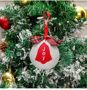 Close-up of grey knitted Christmas ball with red JOY embroidery and plaid bow on tree