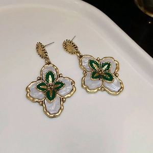 Détail de boucles d'oreilles vintage avec cadre doré, incrustation blanc nacré et trèfle vert