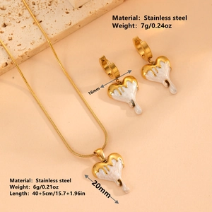 Golden heart-shaped stainless steel jewelry set with white dripping enamel on peach background