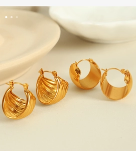 Close-up of golden shell textured and smooth polished hoop earrings on a beige surface
