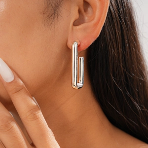 Close-up of minimalist silver rectangular link earrings worn by a model in soft lighting