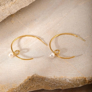 Detail view of gold-plated twisted C-shaped earrings with white pearls on natural stone