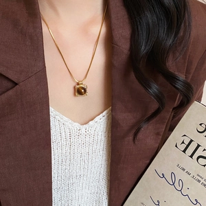 Detailed close-up of 18K gold plated necklace with tiger eye stone pendant on woman's neck
