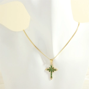 Close-up of 18K gold cross necklace featuring green marquise stones and white zircons