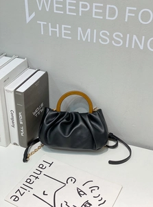 Detail of black pleated cloud bag featuring amber handle and gold metal chain strap