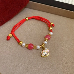Dettaglio del bracciale intrecciato rosso con perla dorata e ciondolo a cavallo
