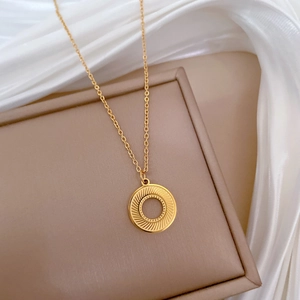 Detail of gold rotating circular pendant with concentric texture on a fine chain