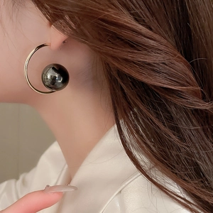 Macro shot of model wearing a gold C-shape earring with a large glossy black pearl detail