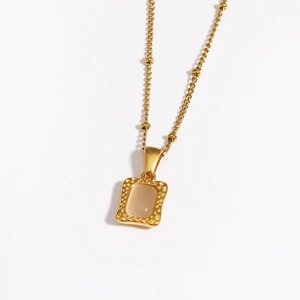 Detailopname van een gouden parfumflesje hanger met beige steen aan een bolletjesketting