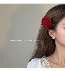 Close-up of a vintage red velvet rose hairpin with green leaf detail on a model
