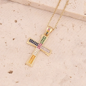 Dettaglio del ciondolo a croce in oro 18K con pietre preziose colorate su sfondo pietra