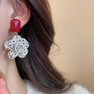 Detailed view of red stud earrings with white polka dot flower charms on a model