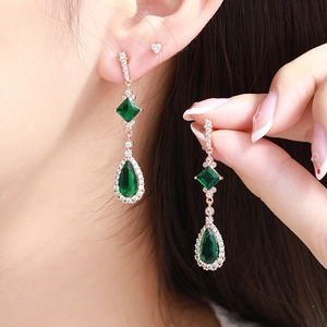 Macro detail of emerald-cut and teardrop green gemstones on rose gold long earrings