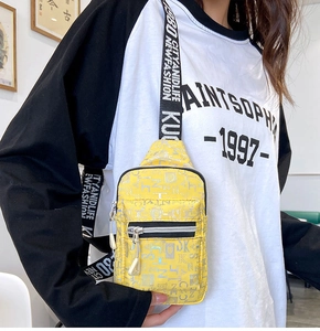 Detail view of yellow crossbody chest bag with silver letters and striped strap
